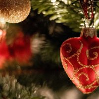 Close up image of Christmas tree with red, heart-shaped ornament in foreground