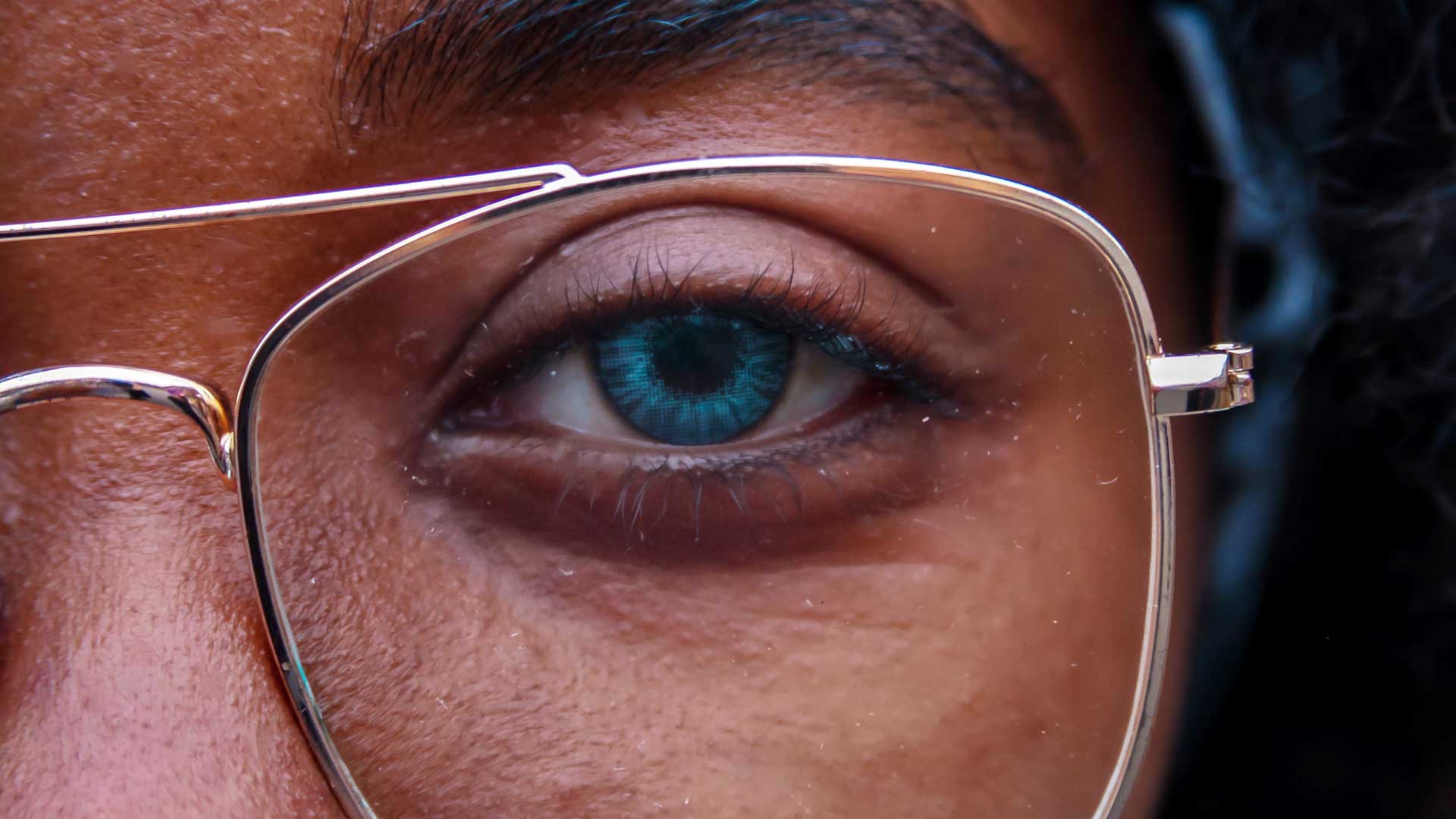 Close-up image of black man with blue eyes wearing clear metallic frame spectacles.