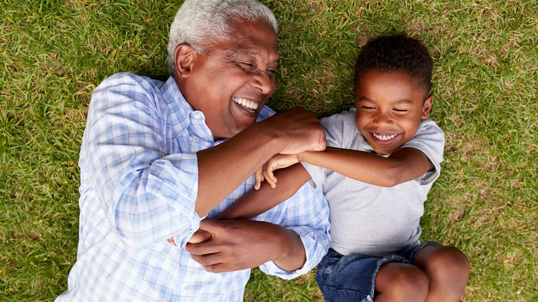 Old man and young boy lying on grass while playing