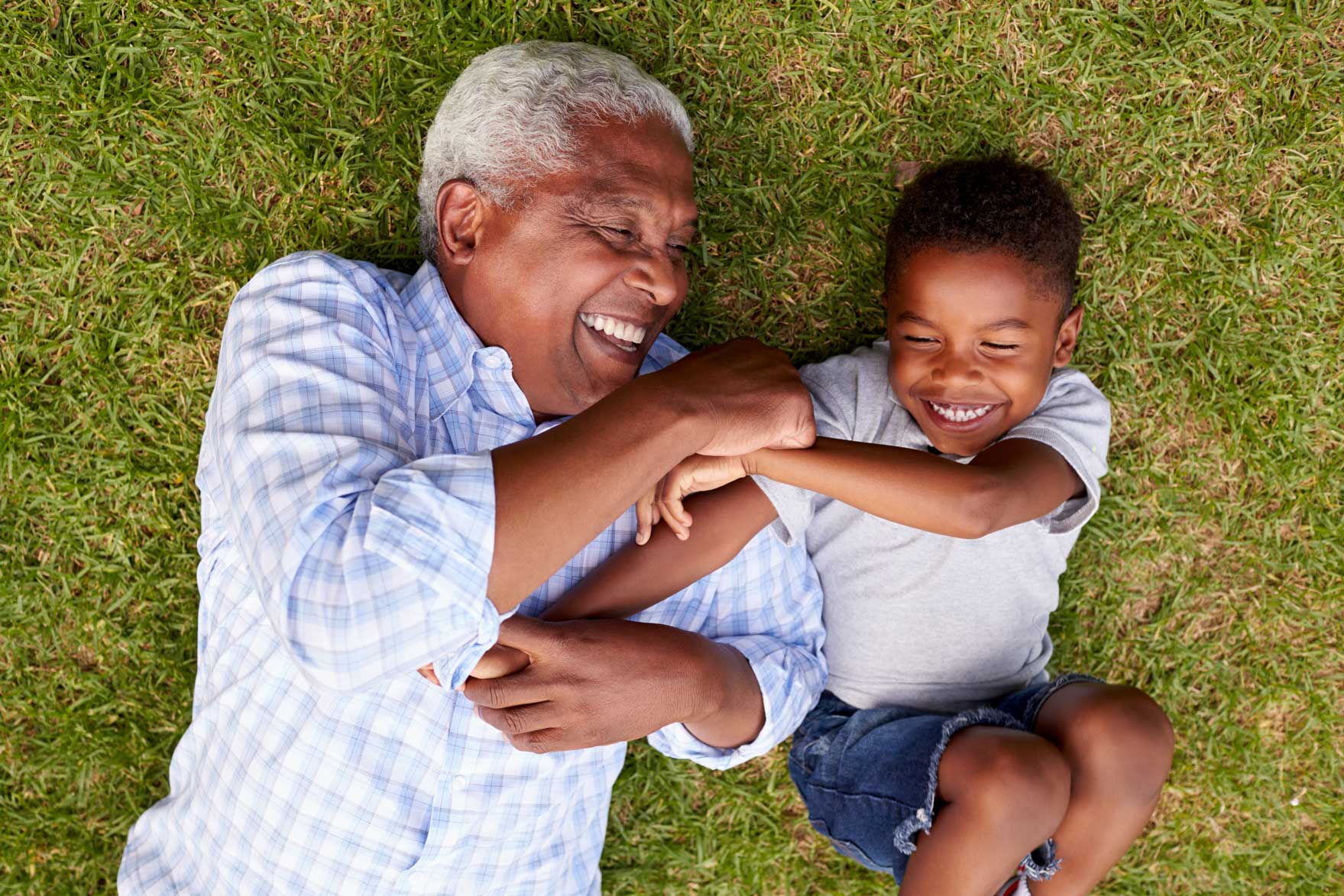 Old man and young boy lying on grass while playing