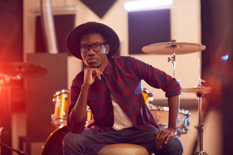An African musician seated infront of drum set holding his chin pensively. | Image: WAKILISHA